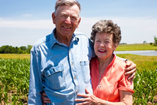 A Proud Hardworking Midwestern Grandmother And Grandfather, Farmers, Stand Proudly Together In Love, On The Family Farm. Vast Expanse Of Open Fertile Land Spreads Out Beyond. Scene Represents &Quot;Down Home&Quot; Values, Hard Work, Love And Americana At Its Best.