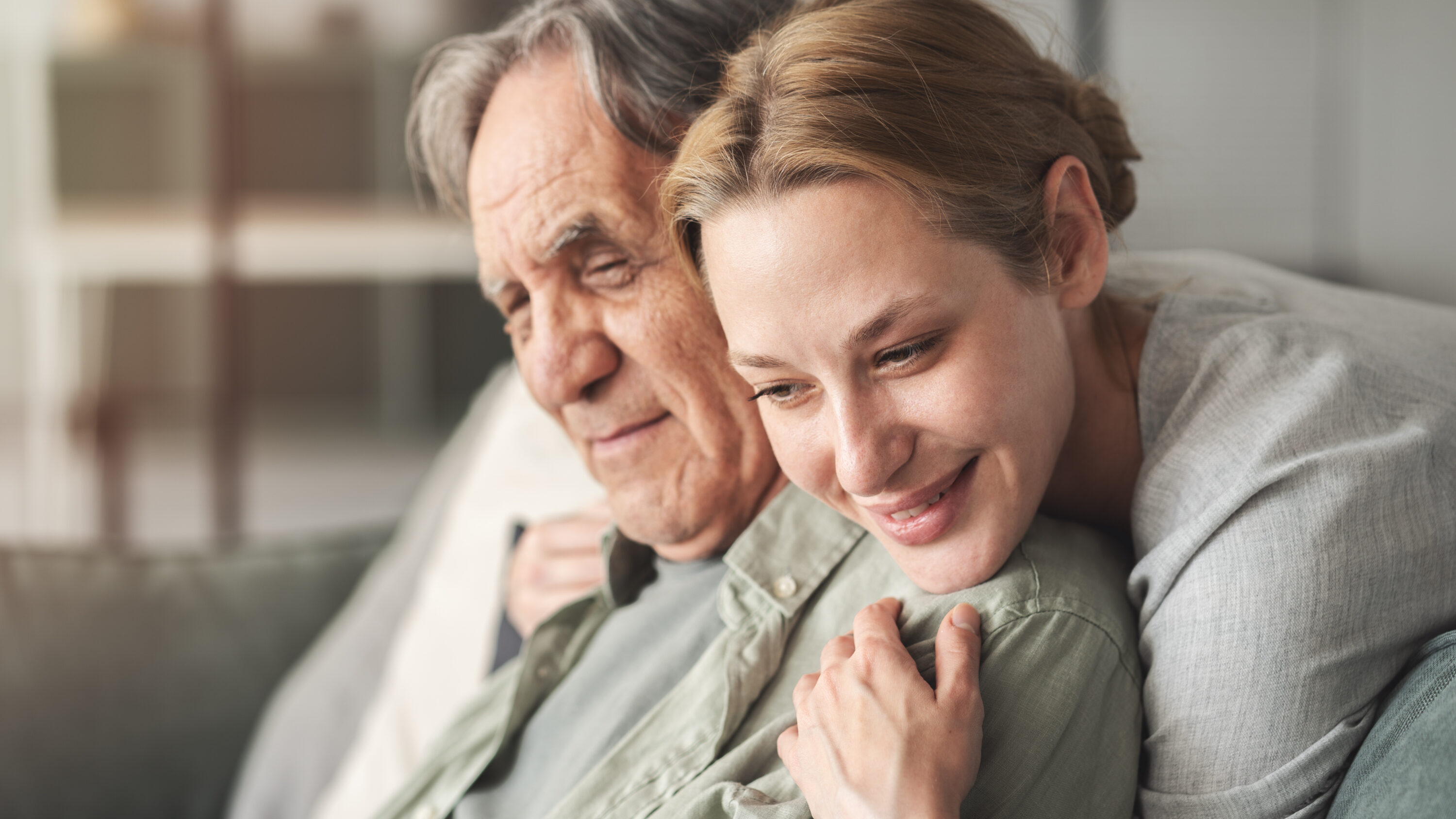 Young woman hugging elderly man on couch