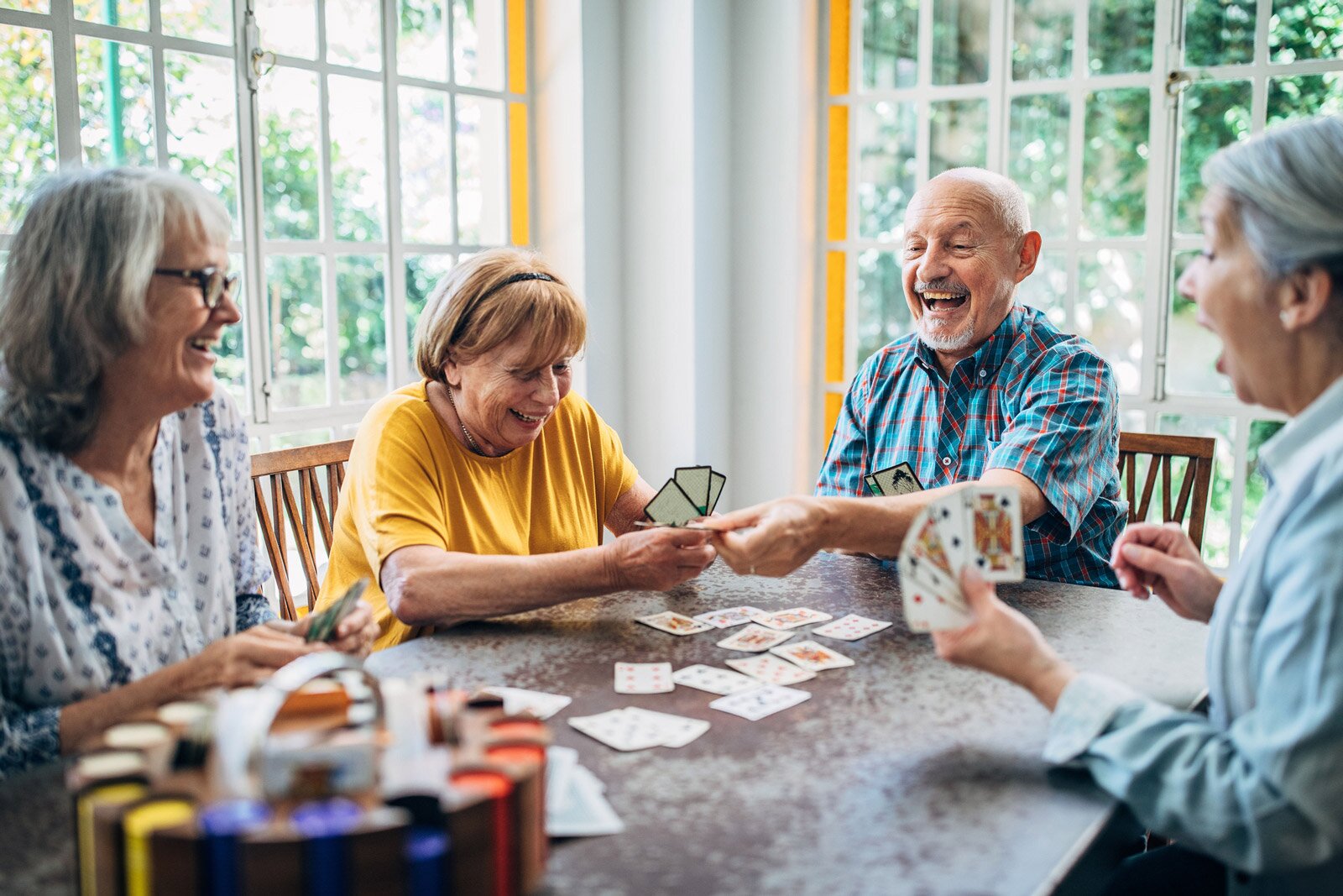 Four seniors laughing while playing cards indoors