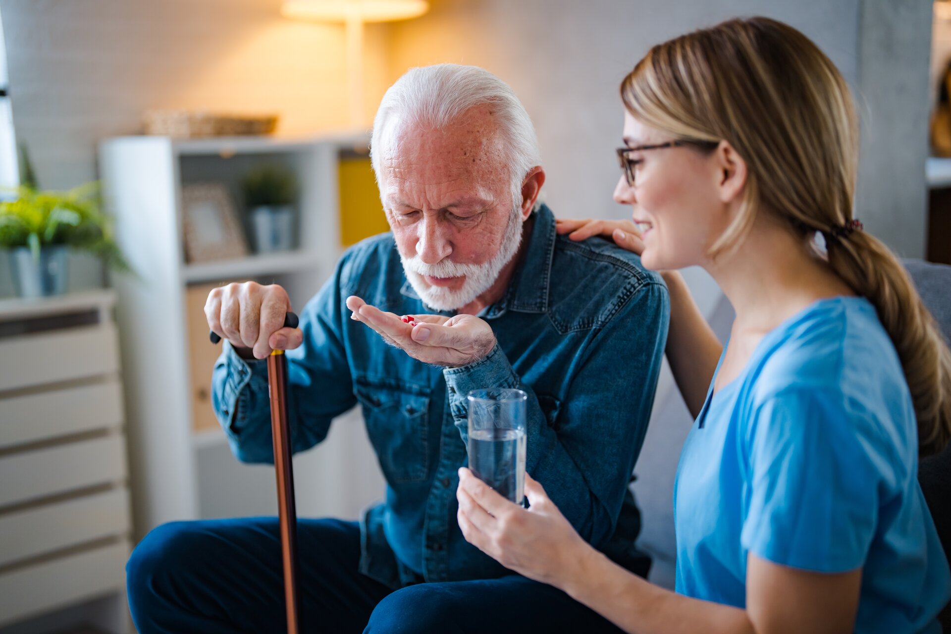 Caregiver assisting elderly man with medication and water