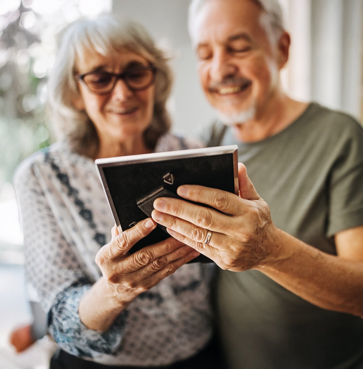 Senior couple smiling at framed photograph indoors
