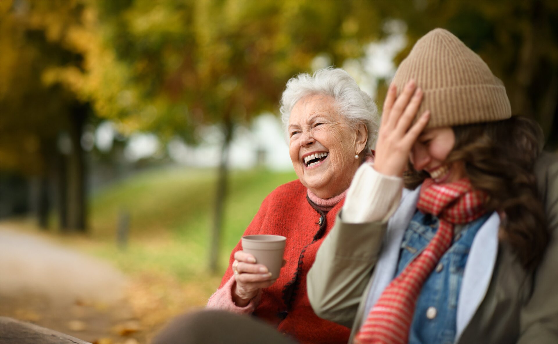 Grandmother and granddaughter laughing on autumn park bench