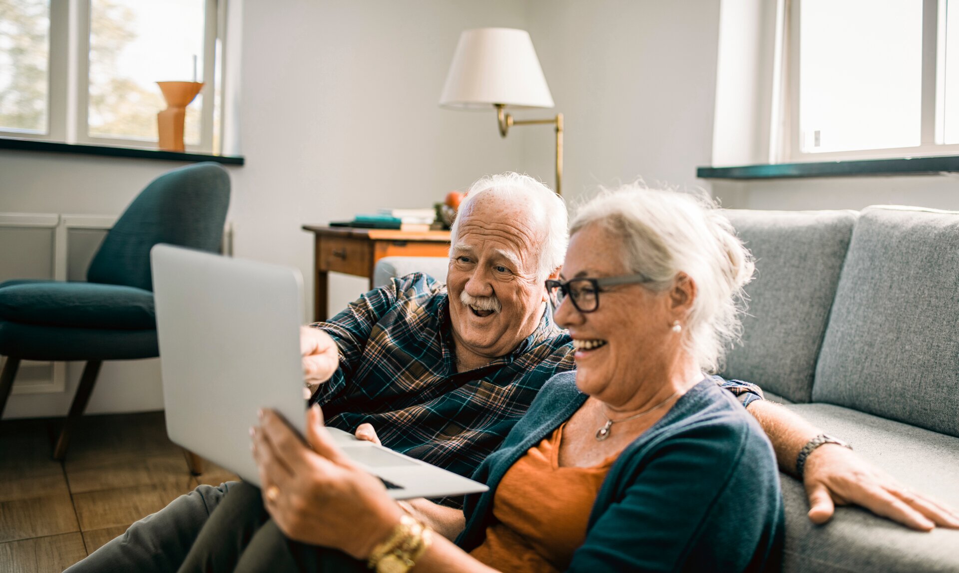 Senior couple smiling at laptop on couch