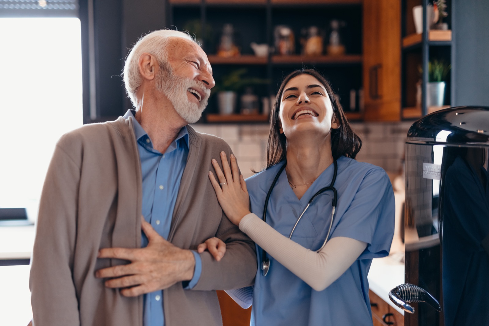 Smiling nurse and elderly man laughing together indoors