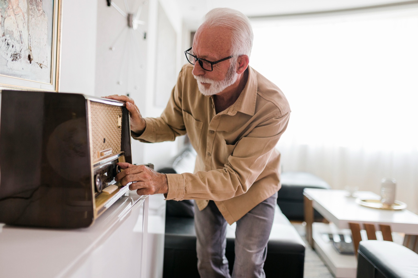 Senior man adjusting vintage radio in living room