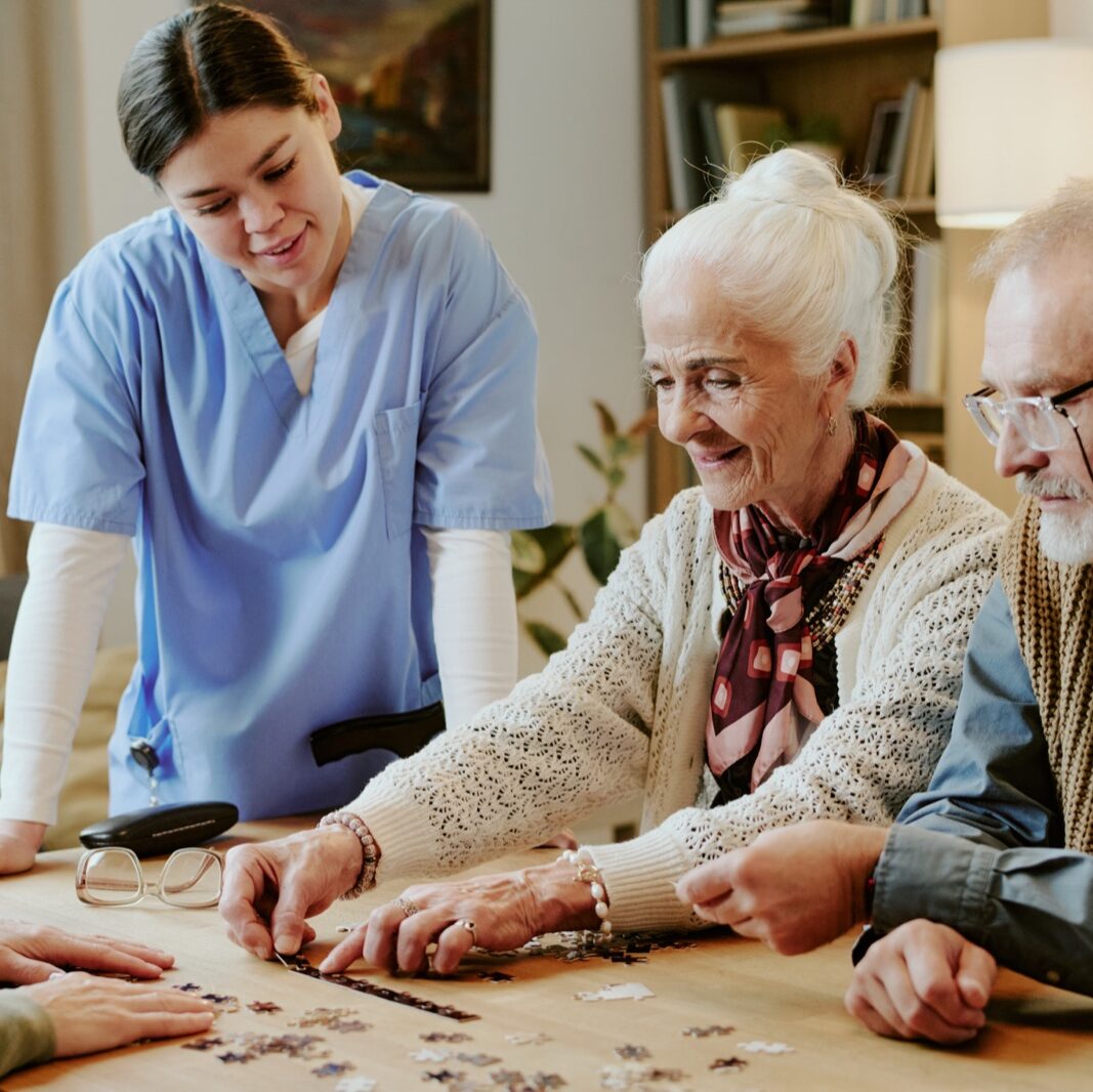 Caregiver helping seniors assemble puzzle at table