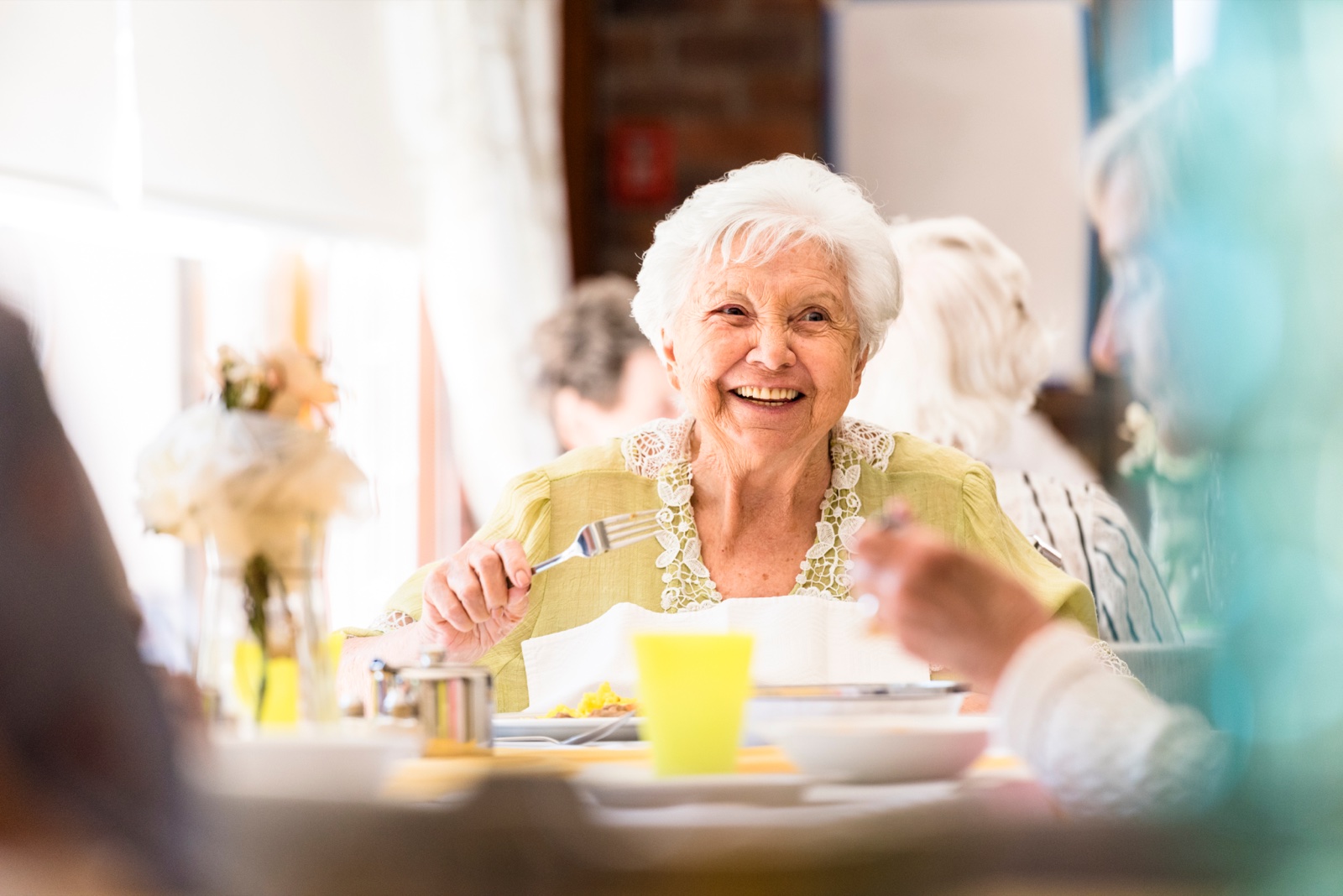 Smiling elderly woman dining with friends indoors